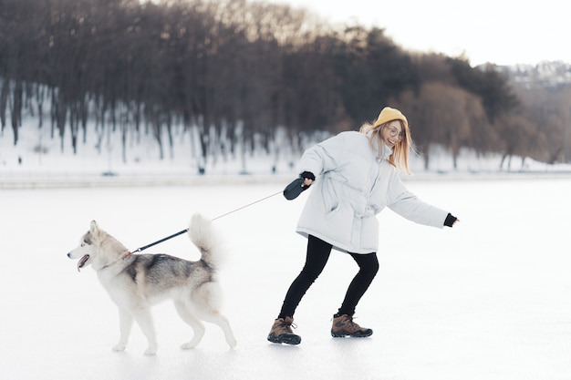 Glückliches junges Mädchen, das mit Siberian Husky Hund im Winterpark spielt