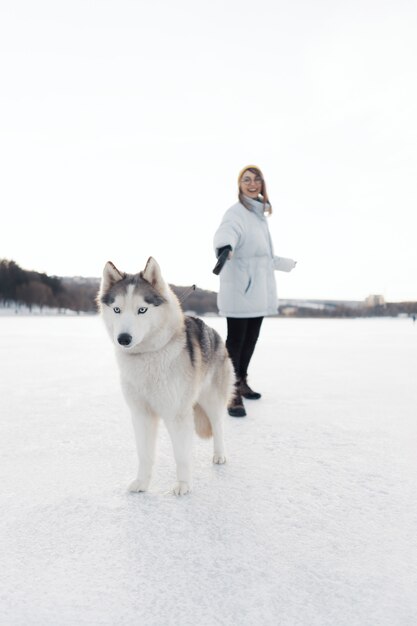 Glückliches junges Mädchen, das mit Siberian Husky Hund im Winterpark spielt