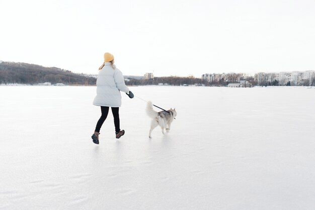 Glückliches junges Mädchen, das mit Siberian Husky Hund im Winterpark spielt