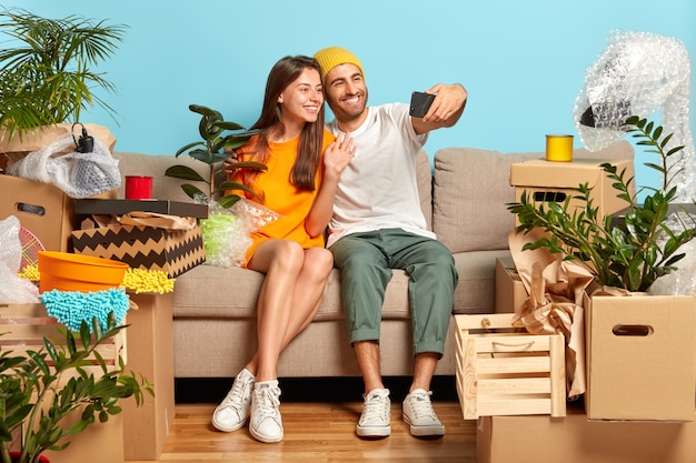 Glückliches junges Paar, das auf der Couch sitzt, umgeben von Kisten