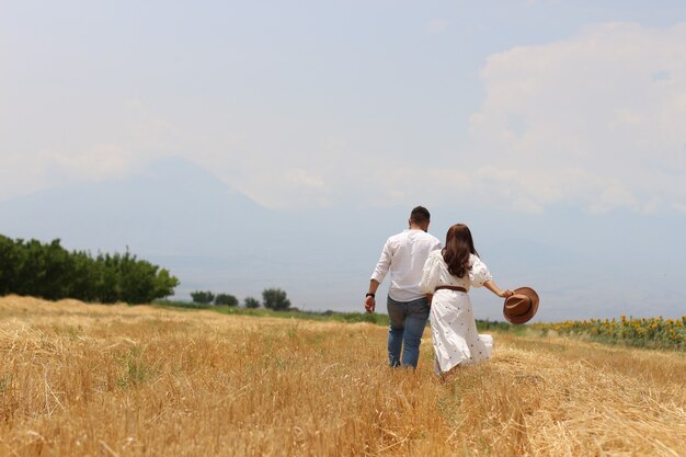 Glückliches junges Paar, das auf einer trockenen Wiese mit blauem Himmel läuft running