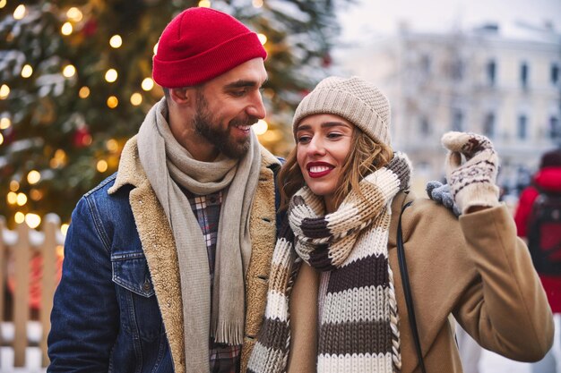Glückliches junges paar, das in der nähe des städtischen weihnachtsbaums spazieren geht