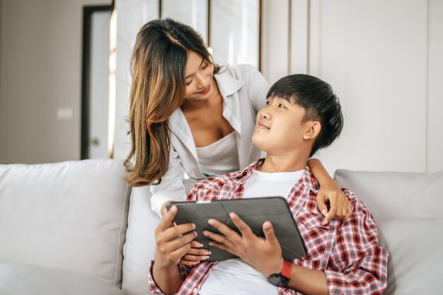 Glückliches junges Paar, das zu Hause auf dem Sofa im Wohnzimmer sitzt, benutzt Tablet mit Glück zusammen glückliches Familienkonzept