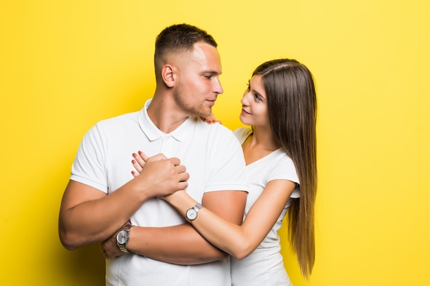 Glückliches junges Paar gekleidet in weißen T-Shirts, die auf gelbem Hintergrund umarmen