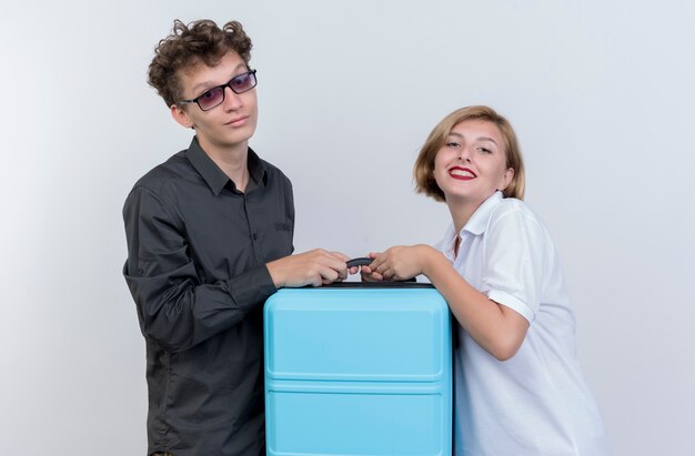 Glückliches junges Paar Touristenmann und -frau, die Koffer halten, der über weiße Wand lächelt