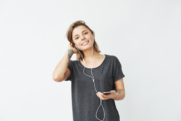 Glückliches junges schönes Mädchen in den Kopfhörern, die Telefon lächelnd halten.