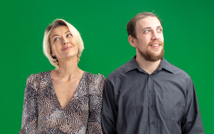 Kostenlose Foto glückliches junges schönes paar mann und frau, die lächelnd fröhlich feiern valentinstag stehen über grüne wand schauen