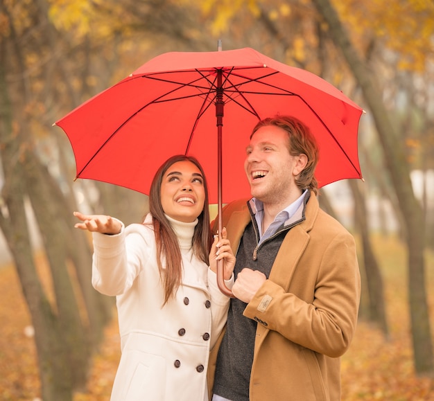 Glückliches kaukasisches Paar, das im Herbst einen Regenschirm im Park hält