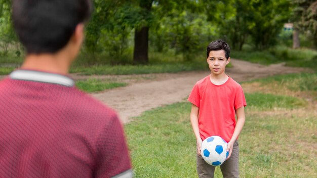 Glückliches Kind im roten Hemd, das mit dem Ball spielt