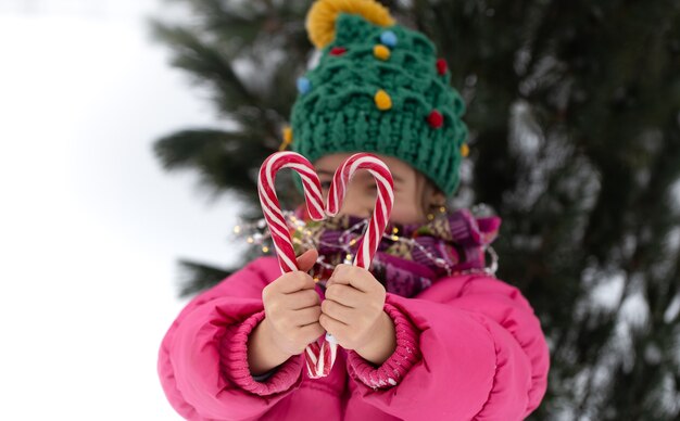 Glückliches Kind mit großen Zuckerstangen unter einem Weihnachtsbaum. Winterferienkonzept.