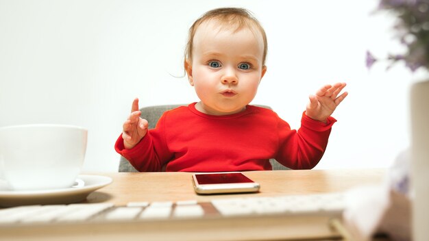 Glückliches Kindbaby, das mit Tastatur des modernen Computers oder des Laptops im weißen Studio sitzt