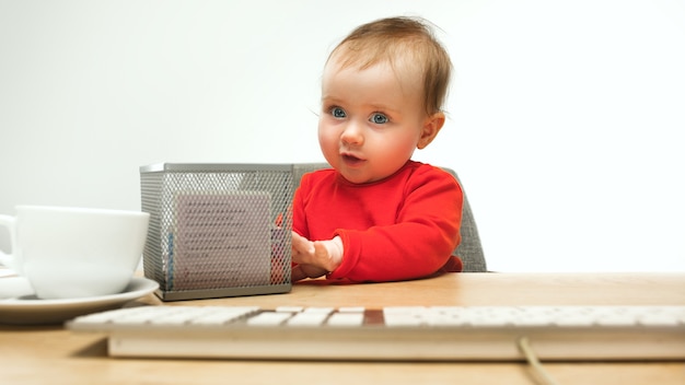 Glückliches Kindbaby, das mit Tastatur des modernen Computers oder des Laptops im weißen Studio sitzt.