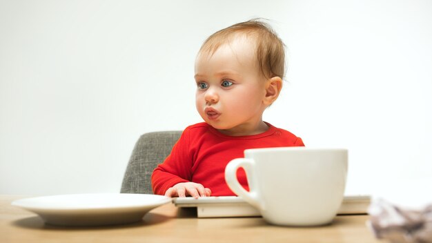 Glückliches Kindbaby, das mit Tastatur des modernen Computers oder des Laptops in Weiß sitzt