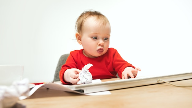 Glückliches kindbaby, das mit tastatur des modernen computers oder des laptops lokalisiert auf einem weißen studio sitzt.
