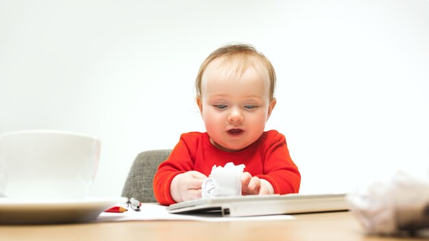Glückliches Kindbaby, das mit Tastatur des modernen Computers oder des Laptops lokalisiert auf einem weißen Studio sitzt.