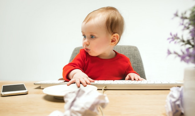 Glückliches kindbaby-kleinkind, das mit tastatur des computers auf einem weißen sitzt