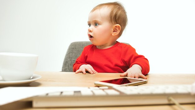 Glückliches Kindbaby-Kleinkind, das mit Tastatur des Computers lokalisiert auf einem weißen sitzt