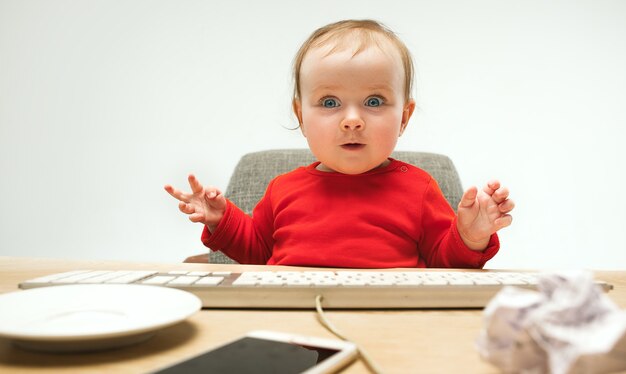 Glückliches Kindbaby-Kleinkind, das mit Tastatur des Computers lokalisiert auf einem weißen sitzt