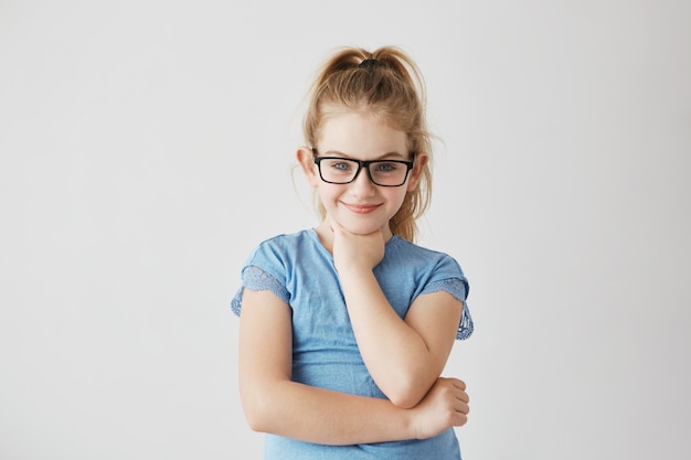 Glückliches kleines blondes Mädchen mit blauen Augen mit glücklichem und friedlichem Ausdruck in der brandneuen schwarzen Brille.