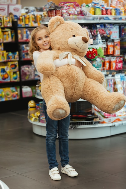 Kostenloses Foto glückliches kleines mädchen, das großen teddybären hält