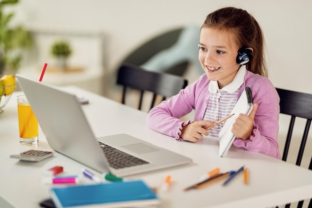 Glückliches kleines Mädchen, das Online-Unterricht mit einem Lehrer über Laptop hat