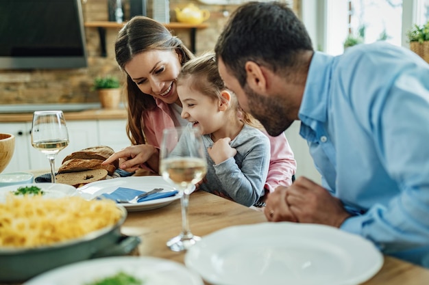 Glückliches kleines Mädchen, das Spaß mit ihren Eltern während einer Mahlzeit am Esstisch hat