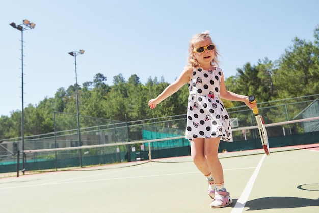 Glückliches kleines Mädchen, das Tennis spielt. Sommersport