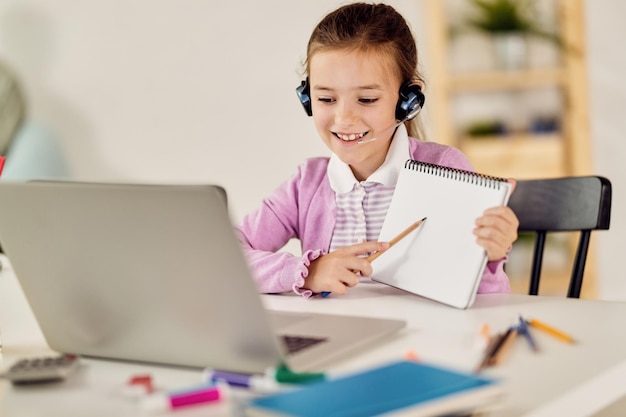Glückliches kleines Mädchen, das Videoanrufe tätigt, während es Online-Unterricht über Laptop hat