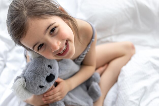 Glückliches kleines Mädchen mit Stofftierkoala im Bett