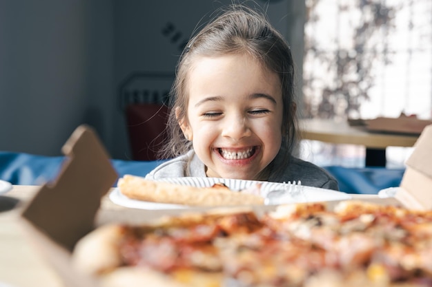 Glückliches kleines Mädchen schaut Pizza mit Appetit an