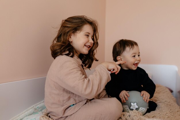 Glückliches kleines Mädchen spielt mit ihrem kleinen Bruder zu Hause in den Betten Kleine Schwester mit ihrem kleinen Bruder Kleinkind Kind Familie mit Kindern zu Hause