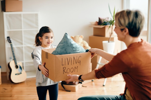 Glückliches kleines Mädchen und ihre Mutter packen ihre Sachen aus, während sie in ein neues Zuhause ziehen