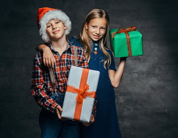 Glückliches kleines Paar, das zur Weihnachtszeit Geschenkboxen umarmt und hält. Auf dunklem Hintergrund.