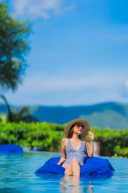 Glückliches Lächeln der schönen jungen asiatischen Frau des Porträts entspannen sich im Swimmingpool am neary Seeozeanstrand des Hotelerholungsortes auf blauem Himmel