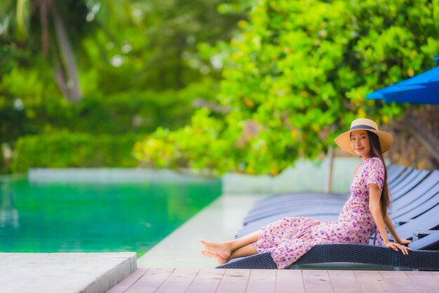 Glückliches Lächeln der schönen jungen asiatischen Frau des Porträts entspannen sich im Swimmingpool am neary Seeozeanstrand des Hotelerholungsortes auf blauem Himmel