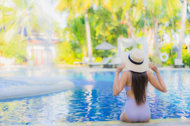 Glückliches Lächeln der schönen jungen asiatischen Frau des Porträts entspannen sich um Swimmingpool im Freien