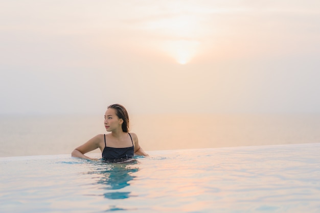Glückliches Lächeln der schönen jungen asiatischen Frau des Porträts entspannen sich um Swimmingpool im Hotelerholungsort