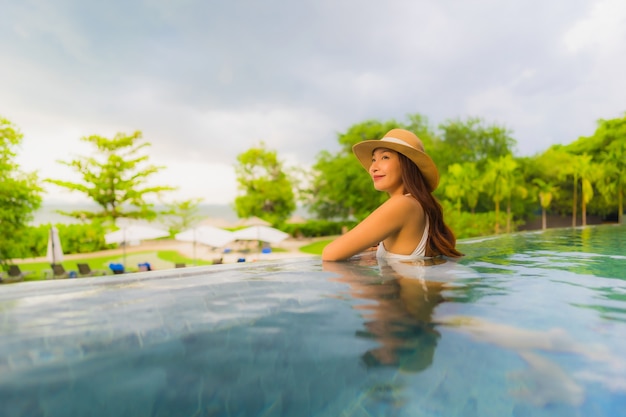 Glückliches Lächeln der schönen jungen asiatischen Frauen des Porträts entspannen sich um Swimmingpool im Freien im Hotel