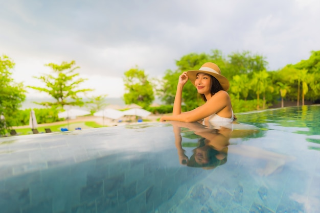 Glückliches Lächeln der schönen jungen asiatischen Frauen des Porträts entspannen sich um Swimmingpool im Freien im Hotel