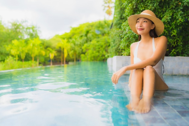 Glückliches Lächeln der schönen jungen asiatischen Frauen des Porträts entspannen sich um Swimmingpool im Freien im Hotel