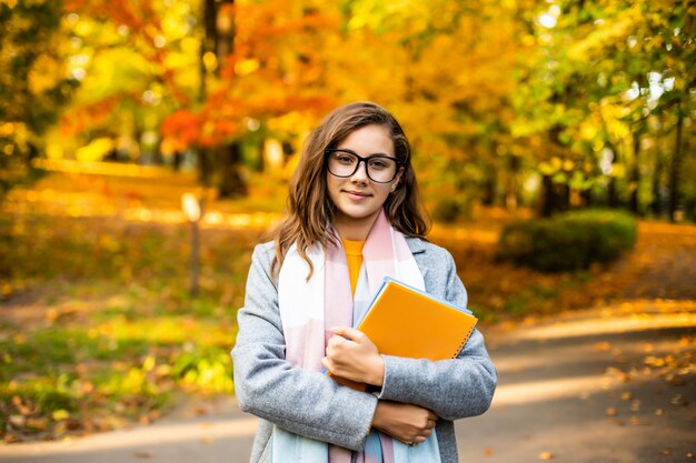 Glückliches lächelndes junges Mädchen des Herbstporträts im Freien mit Heften