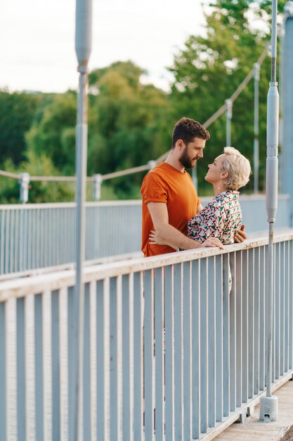 Glückliches lächelndes junges Paar, das auf Brücke umarmt und küsst