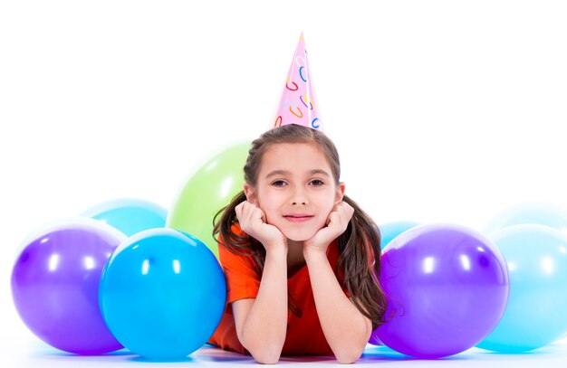 Glückliches lächelndes Mädchen im orangefarbenen T-Shirt, das auf dem Boden mit bunten Luftballons liegt - lokalisiert auf einem Weiß.