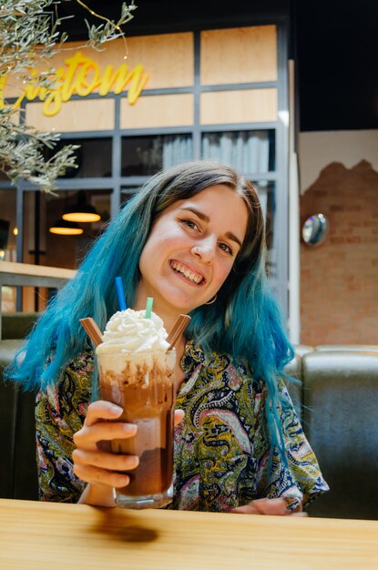Glückliches Mädchen, das mit einem großen Schokoladenmilchshake in einem Kaffeegeschäft lächelt
