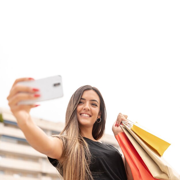 Glückliches Mädchen, das selfie mit Papiertüten nimmt