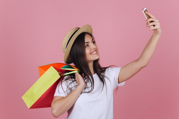 Glückliches Mädchen mit bunten Einkaufstaschen nimmt selfie an ihrem Telefon