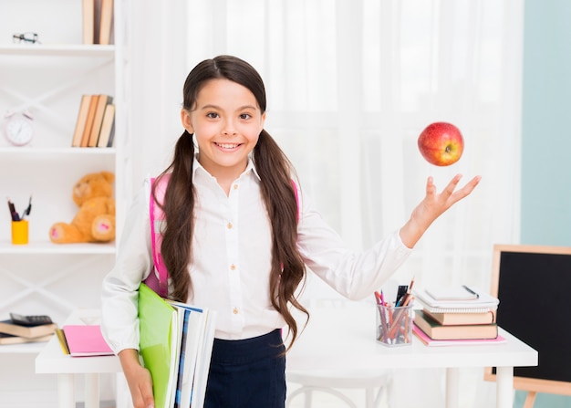 Glückliches Mädchen mit dem Rucksack, der Apfel wirft