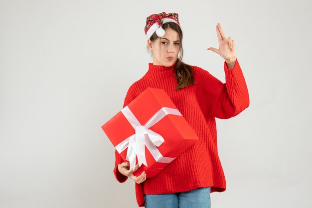 glückliches Mädchen mit Weihnachtsmütze, die Geschenk hält, das Fingerpistole auf Weiß macht