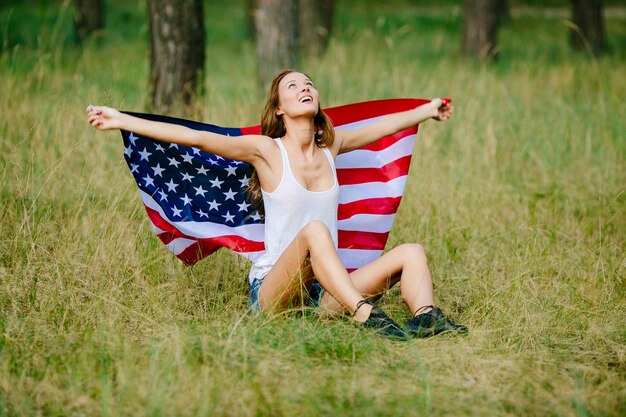 Glückliches Mädchen sitzt auf dem Gras mit der amerikanischen Flagge