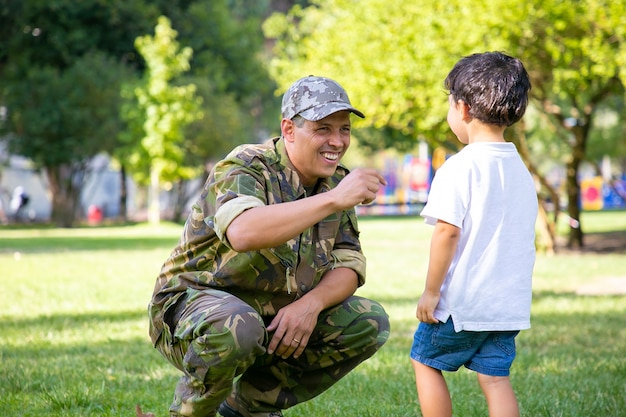 Glückliches militärisches Vatertreffen mit Sohn nach Missionsreise. Junge, der zu Papa geht, der Tarnuniform im Park trägt. Familientreffen oder Rückkehr nach Hause Konzept